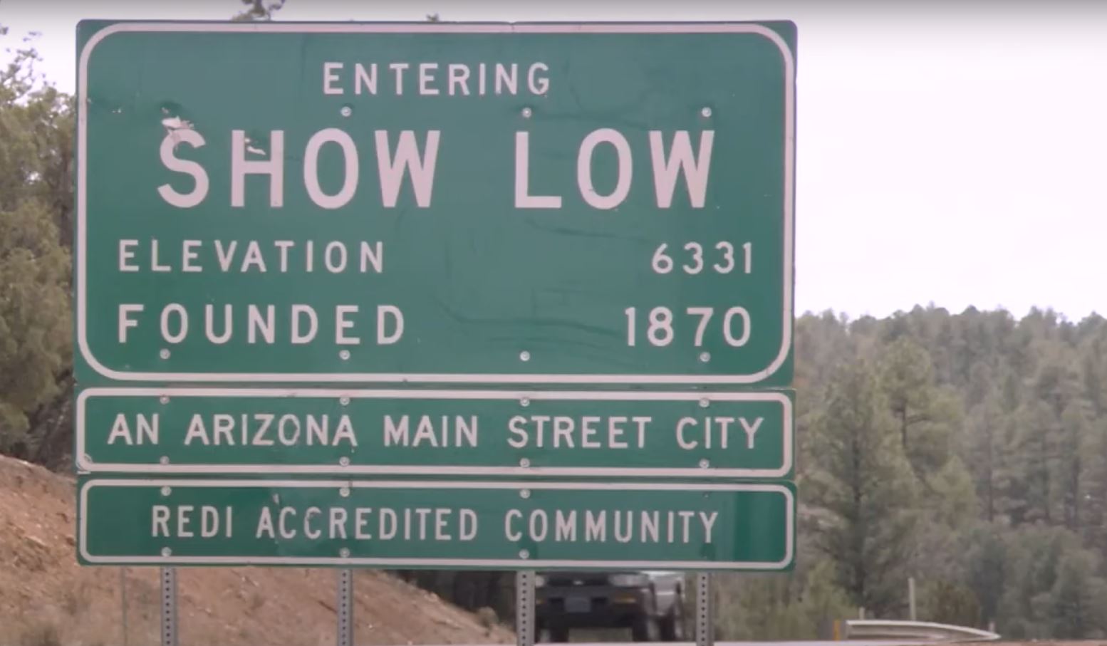 A green sign that says entering Show Low. It lists the elevation and the date Show Low was founded.